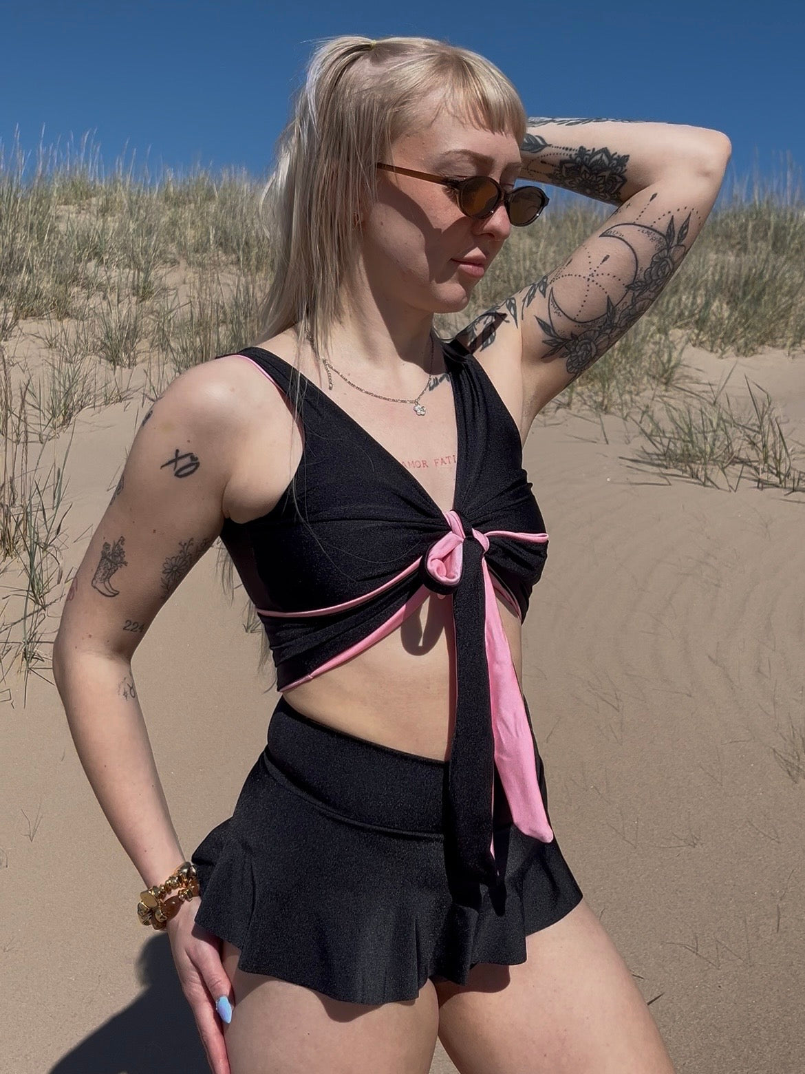 Veera Susanna Design suunnittelijan Ilo bikinimalli, missä on kietaisutoppi sekä bikinin minihameellinen alaosa. Bikinit ovat kuvassa värissä musta. Kuva otettu Porin yyterin hiekkasärkillä.  