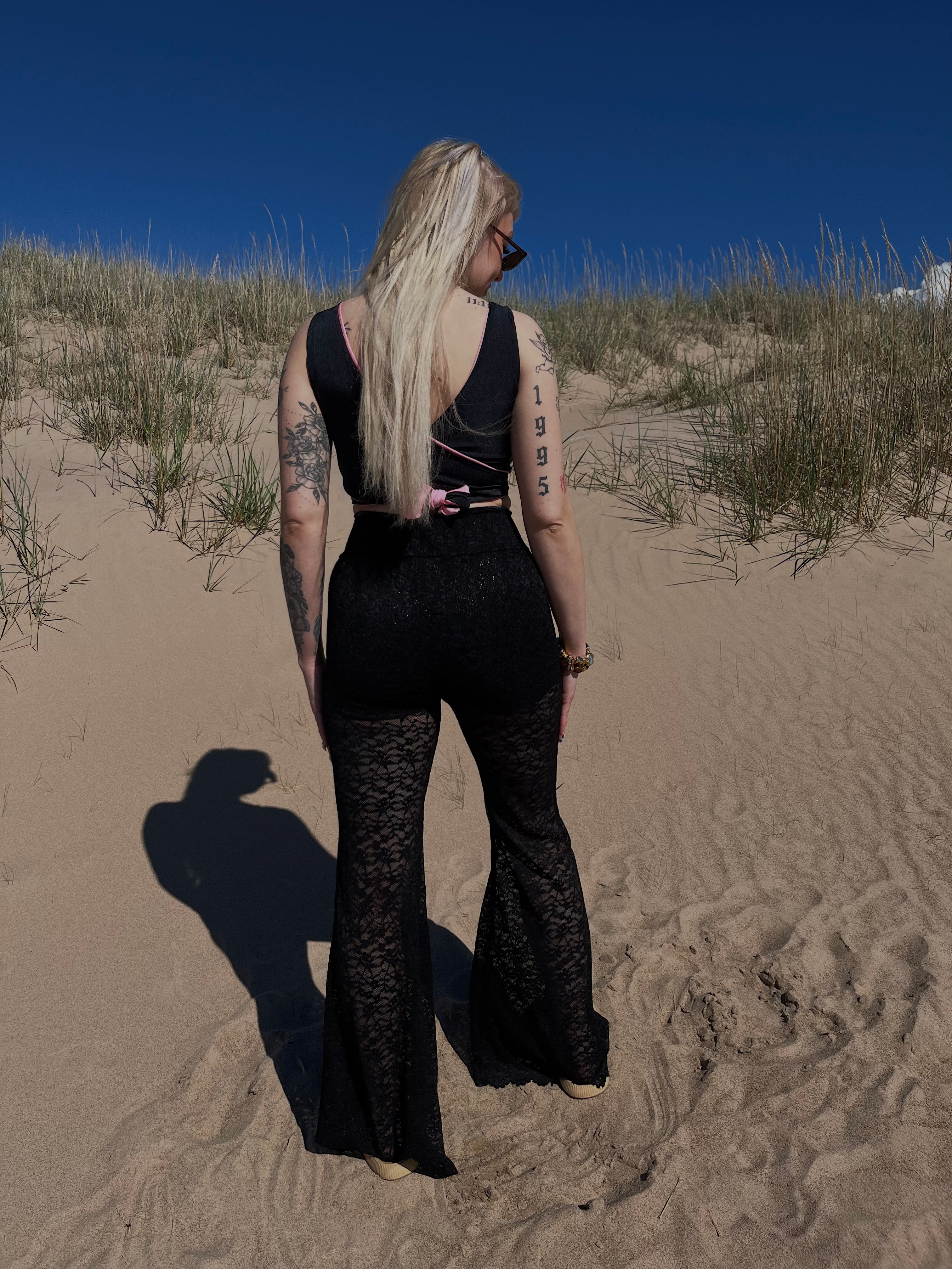 Veera Susanna Design merkin samettiset mini-mallin shortsit sekä pitsihousut yhdistettynä. Mustien shortsien painatettu liekkikuviointi kimaltelee pitsihousujen läpi. Kuva housujen takapuolelta. 