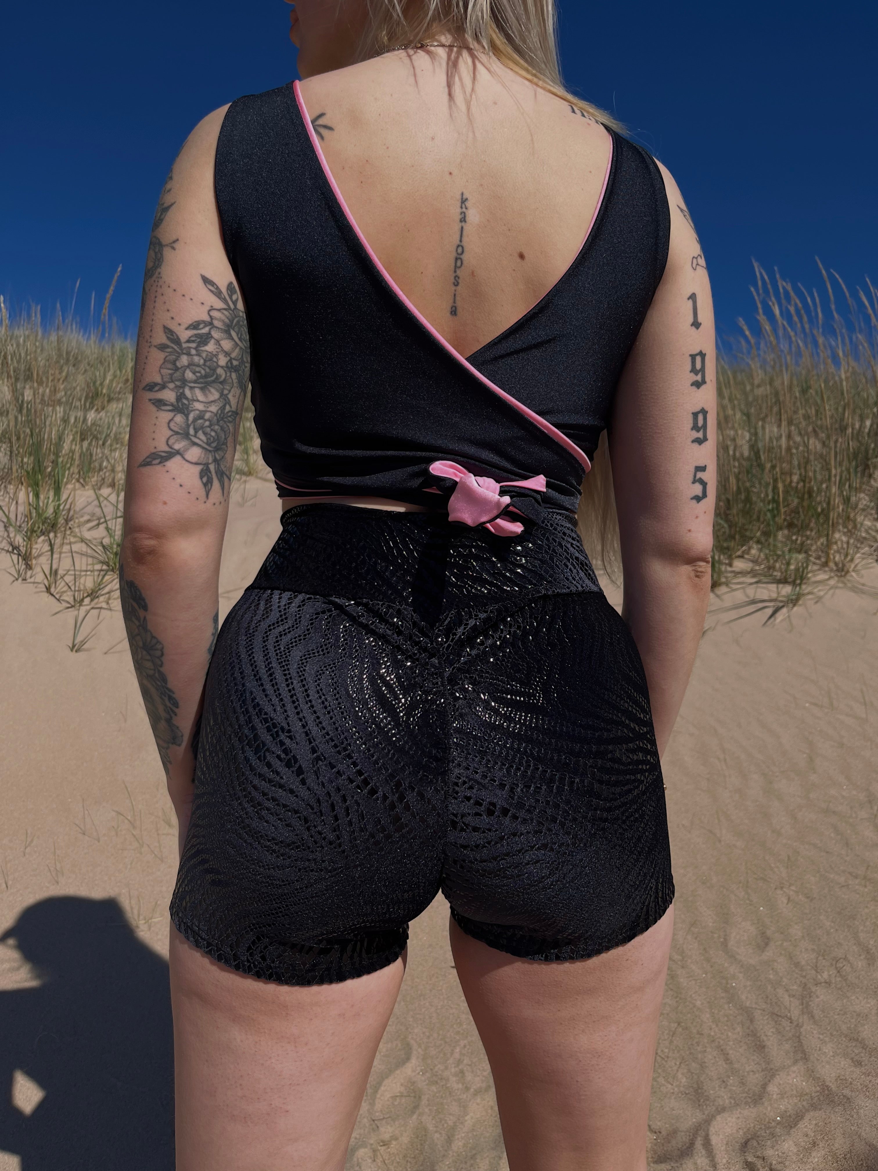 Veera Susanna Design merkin mustat samettiset minishortsit, mustalla painatetulla liekkikuviolla. Kuviointi kiiltää aurinkossa. Kuva otettu shortisen takaa, jossa näkyy shortsien takasaumaan lisätty rypytys.