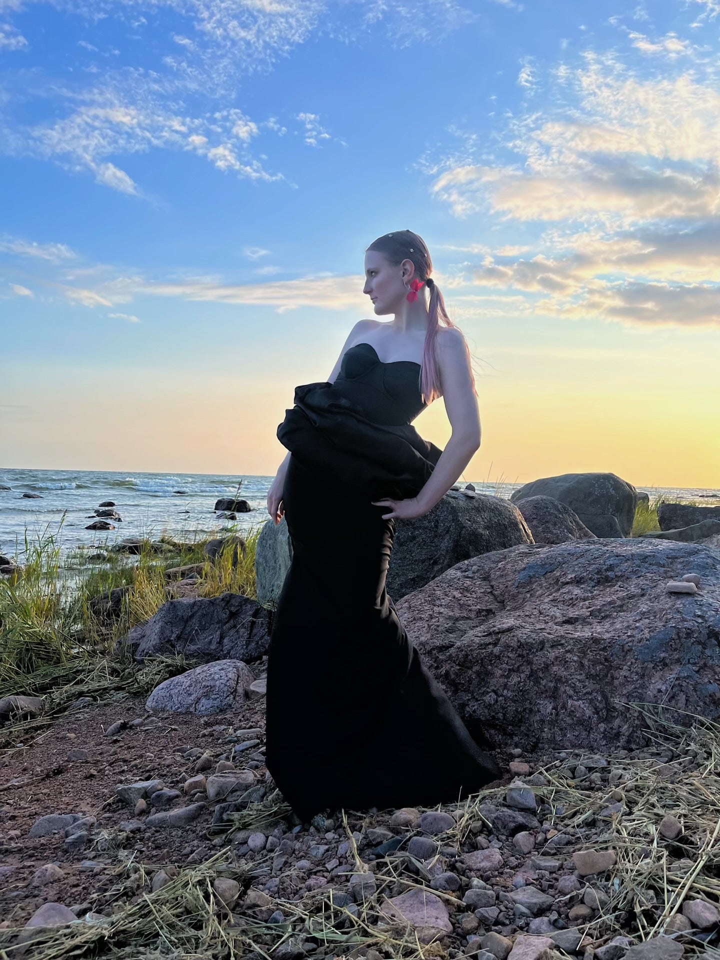 Veera Susanna Designin suunnittelema elegantti iltapuku, musta, jossa vyötäröllä pilveä kuvastava vyö. Kuvassa vaatesuunnittelija itse ,Veera Sepponen. Kuvattu Porin reposaaressa.